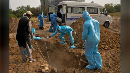 The body of a woman who died from the coronavirus disease (COVID-19), is lowered in a grave as another one is taken out from an ambulance for burial at a graveyard in New Delhi, June 1, 2020. Photo: Danish Siddiqui via Reuters