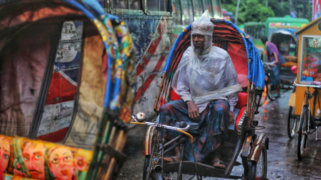 A Rickshaw puller sits idly on his carrier in absence of passengers amid an intermittent rain across the county. Photo: Salahuddin Ahmed/TBS 