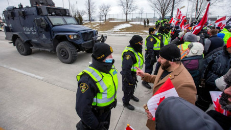 Protesters interact with police officers, who stand guard on a street after Windsor Police said that they are starting to enforce a court order to clear truckers and supporters who have been protesting against coronavirus disease (COVID-19) vaccine mandates by blocking access to the Ambassador Bridge, which connects Detroit and Windsor, in Windsor, Ontario, Canada February 12, 2022. REUTERS/Carlos Osorio