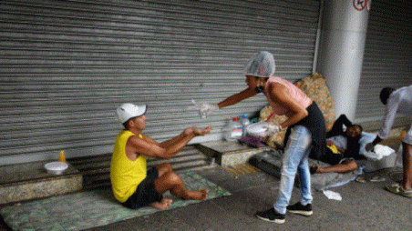 A member of a group of residents of the Chapeu Mangueira slum, sprays alcohol on the hand of a homeless person as she delivers him food during the coronavirus disease (COVID-19) outbreak, at Copacabana beach in Rio de Janeiro, Brazil, April 11, 2020. Picture taken April 11, 2020. REUTERS/Lucas Landau