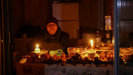 A vendor waits for customers in a store lit with candles during a power outage in Odesa, Ukraine, on December 5, 2022 [Serhii Smolientsev/Reuters]

