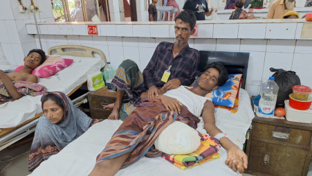 16-year-old Nadim Hossain lying in bed with his father Dulal Hossain and his mother Marium Khatun sitting on the ground at NITOR in Dhaka on 26 July. Photo: Belal Hossen/TBS