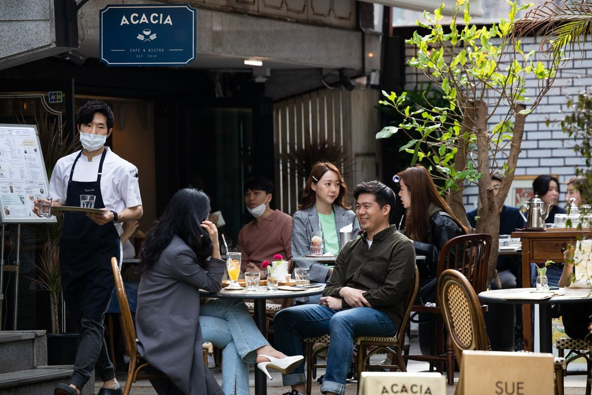 Customers, some wearing protective masks, sit outside a cafe in the Garosu-gil neighborhood of the Gangnam district of Seoul, South Korea on April 18, 2020. 
Photographer: SeongJoon Cho/Bloomberg
