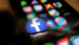 The Facebook logo displayed on a mobile phone is seen through a magnifying glass in this picture illustration taken February 9, 2021. REUTERS/Carlos Jasso/File Photo